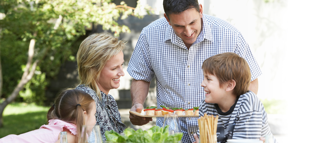 Father serving a tray of food to a women and two children outside