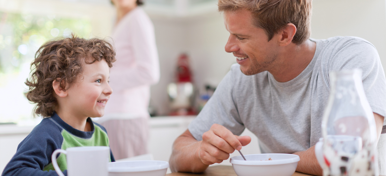 Père souriant à son jeune garçon alors qu’ils déjeunent à la table