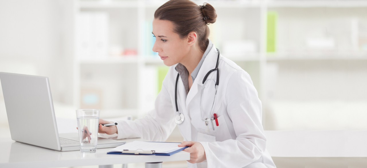 Female doctor sitting at desk looking at laptop